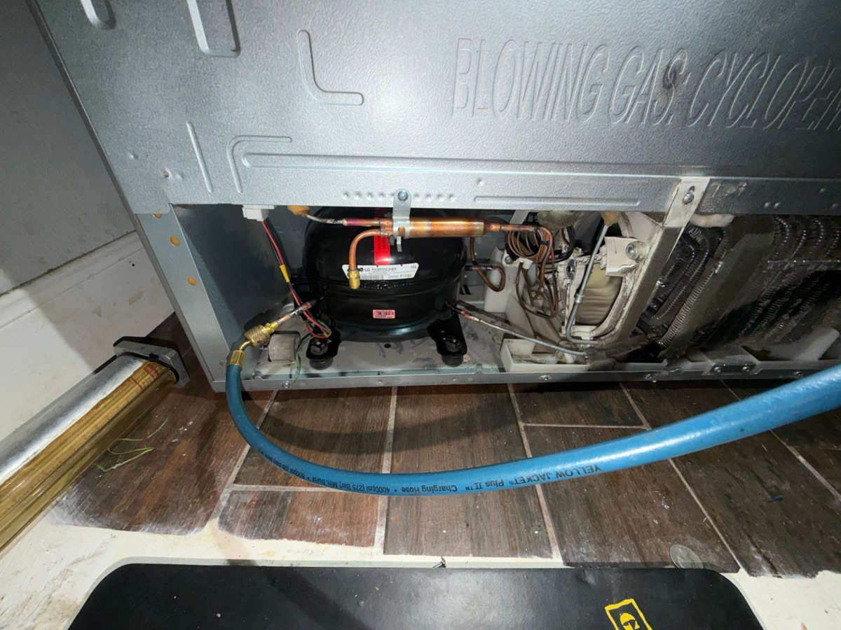 LG compressor and copper tubing at the bottom rear of an LG refrigerator with a blue service hose connected