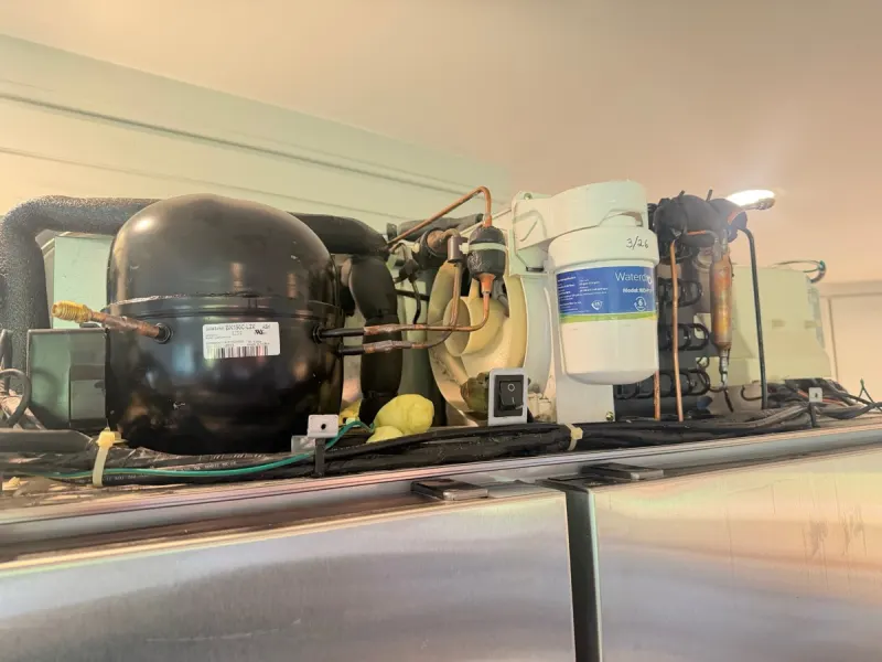 Compressor and copper refrigerant lines on the sealed-system deck on top of a built-in refrigerator