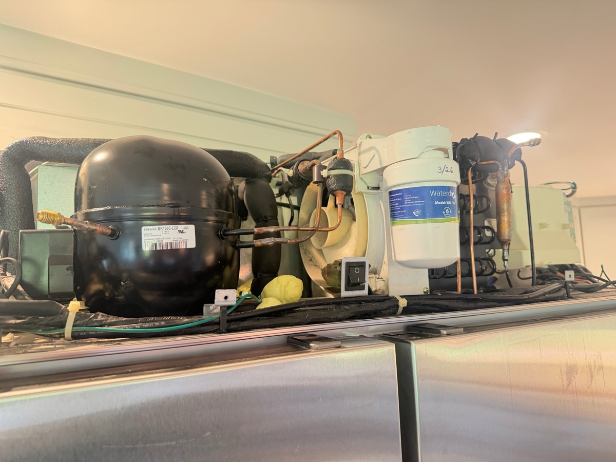 Compressor and copper refrigerant lines on the sealed-system deck on top of a built-in refrigerator
