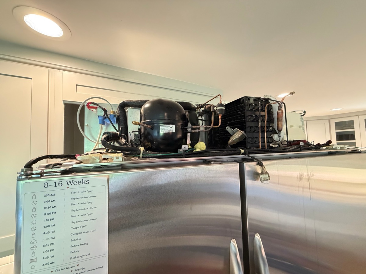 Compressor, condenser coil and copper tubing on top of a built-in refrigerator during a sealed-system repair